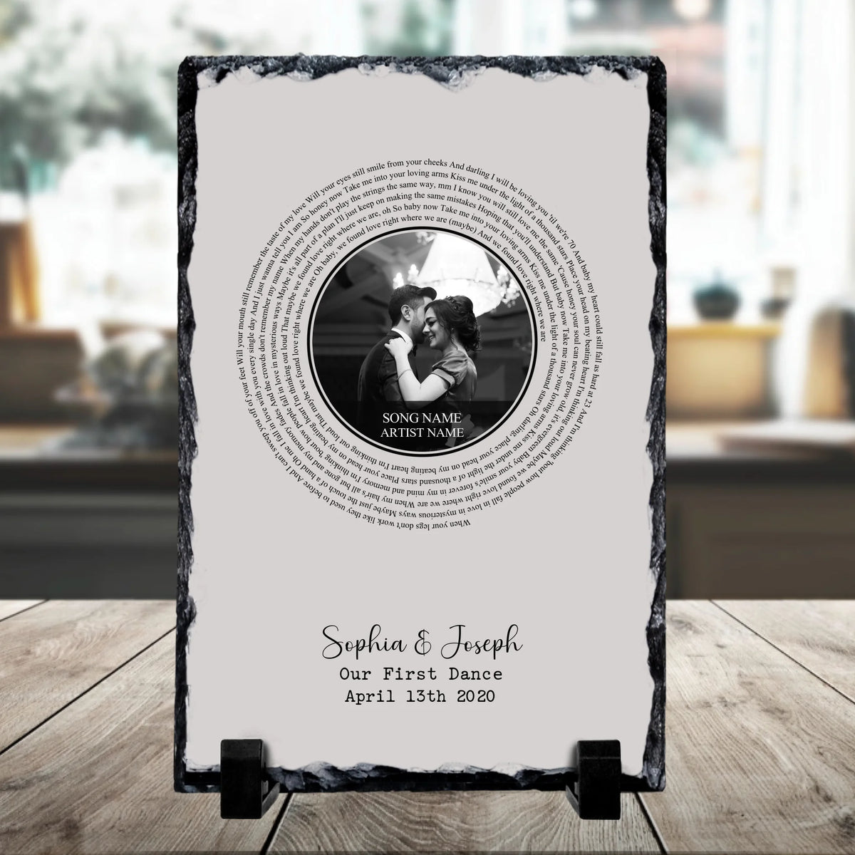 Close-up of personalised wedding slate showing spiral lyrics, black and white couple photo centre, and custom name and date t