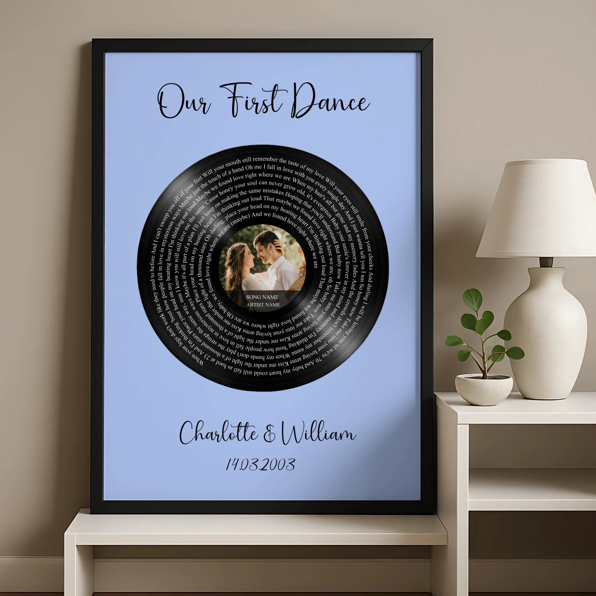 Black framed Our First Dance vinyl record lyrics print on blue, hung on warm beige wall above a sideboard with lamp and small