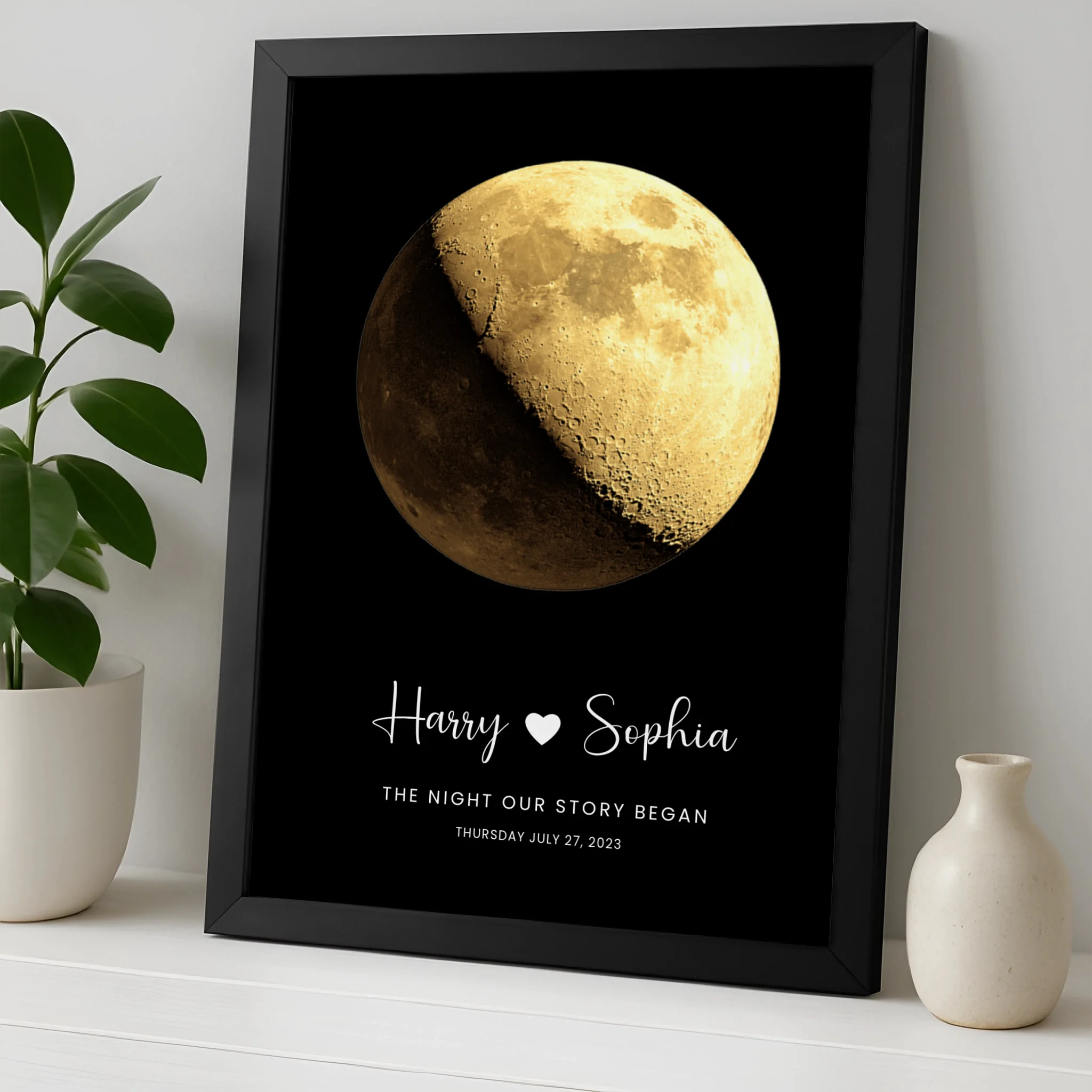 Black framed personalised moon phase print for Harry and Sophia dated July 27 2023, propped on shelf beside a white ceramic v