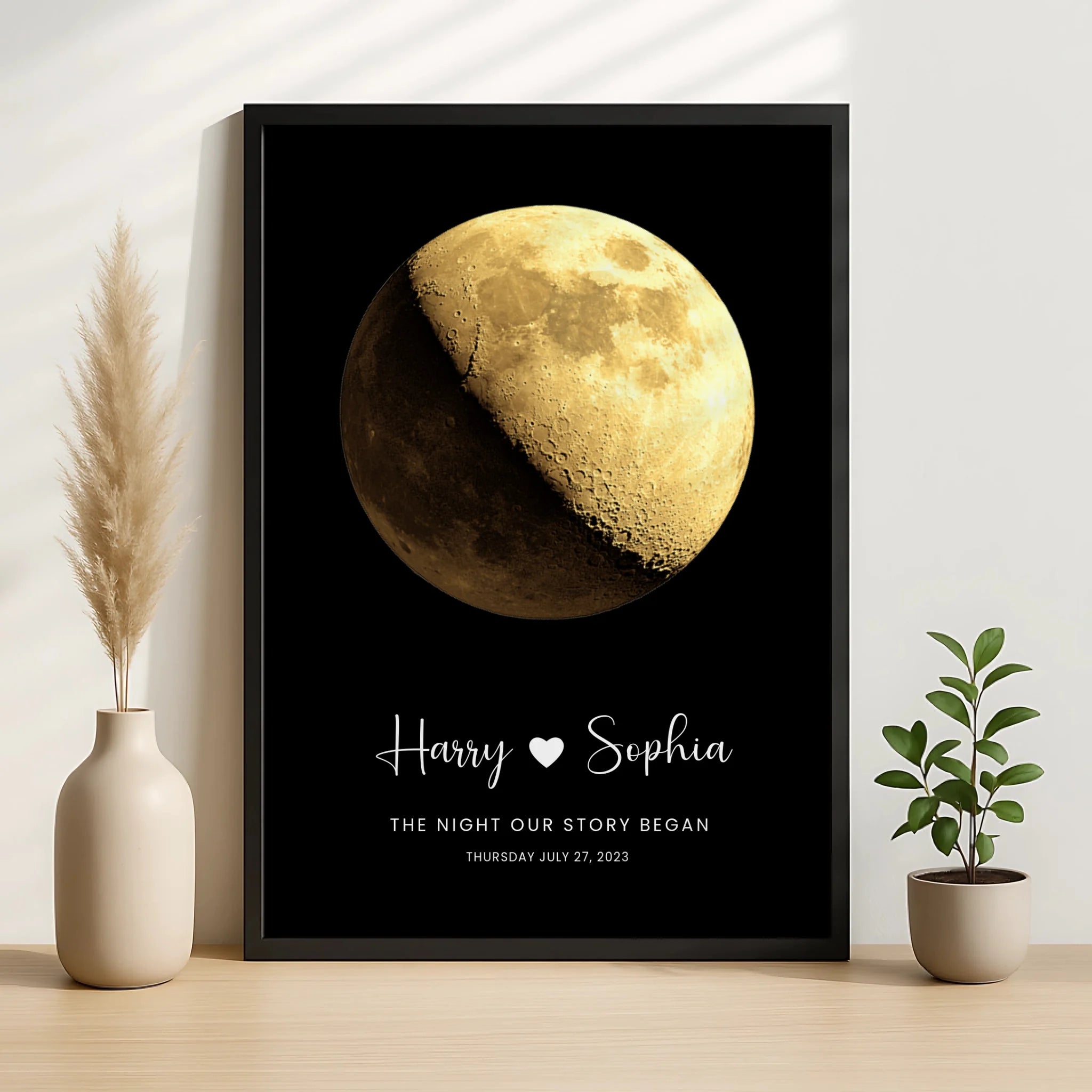 Large black framed moon phase print personalised for Harry and Sophia with date July 27 2023, standing on wooden surface flan