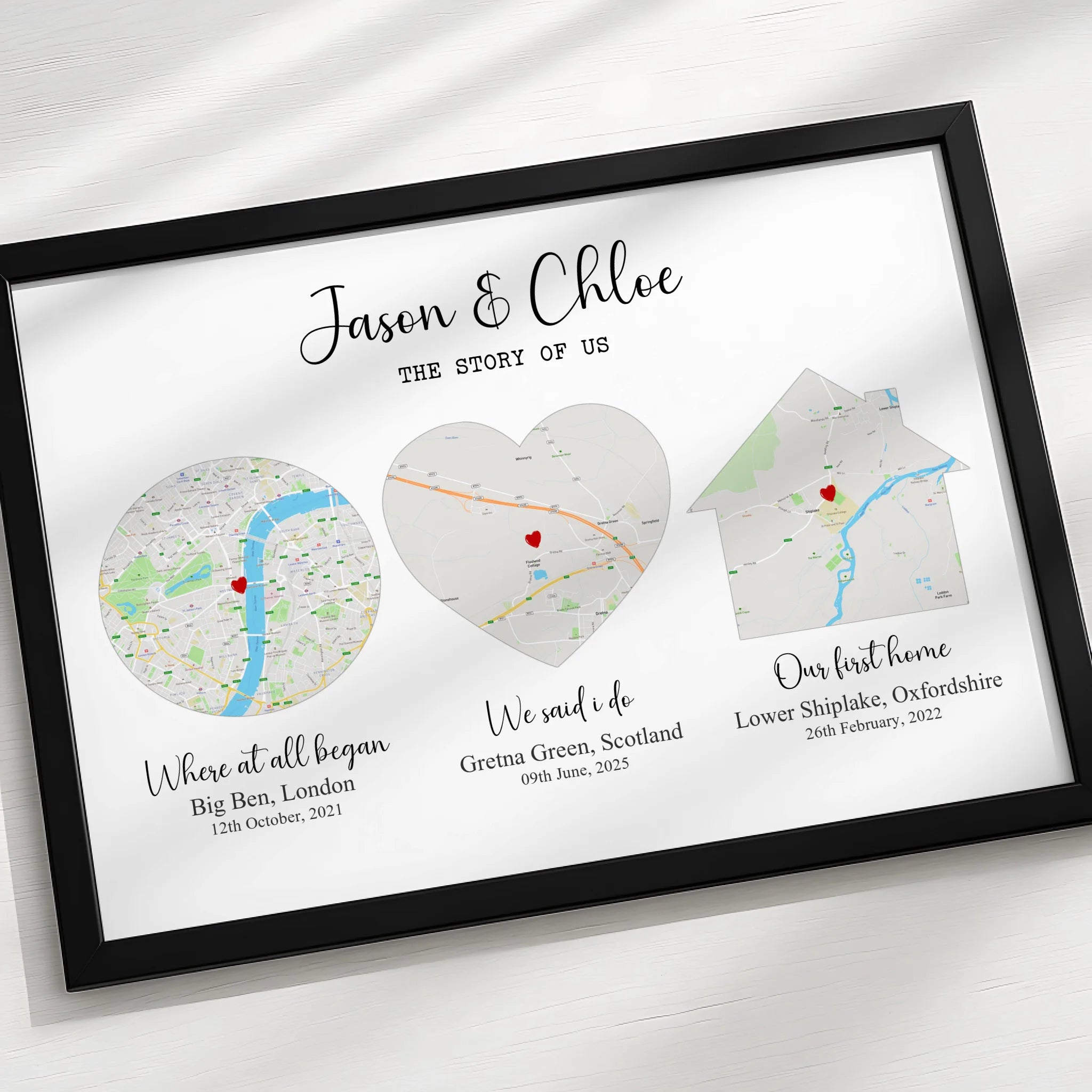 Black framed Story of Us map print shot from above on a white surface, showing three location maps with names and dates benea