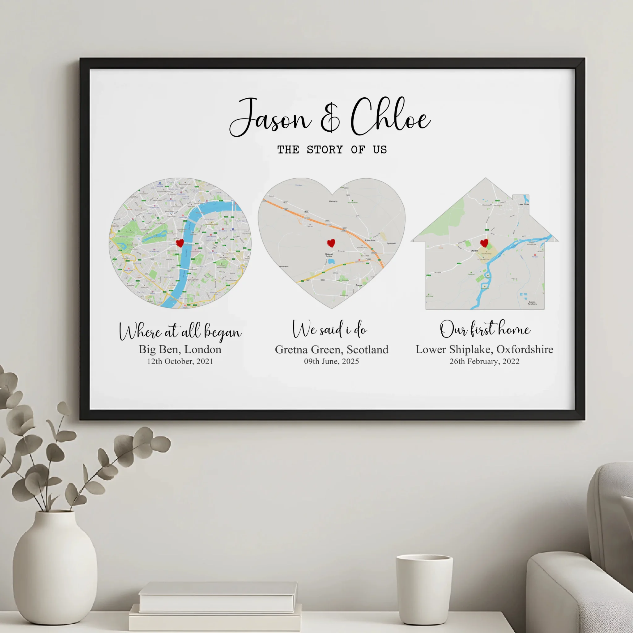 Black framed Story of Us personalised map print hung on a wall above a white vase and cup, three map shapes with place name l