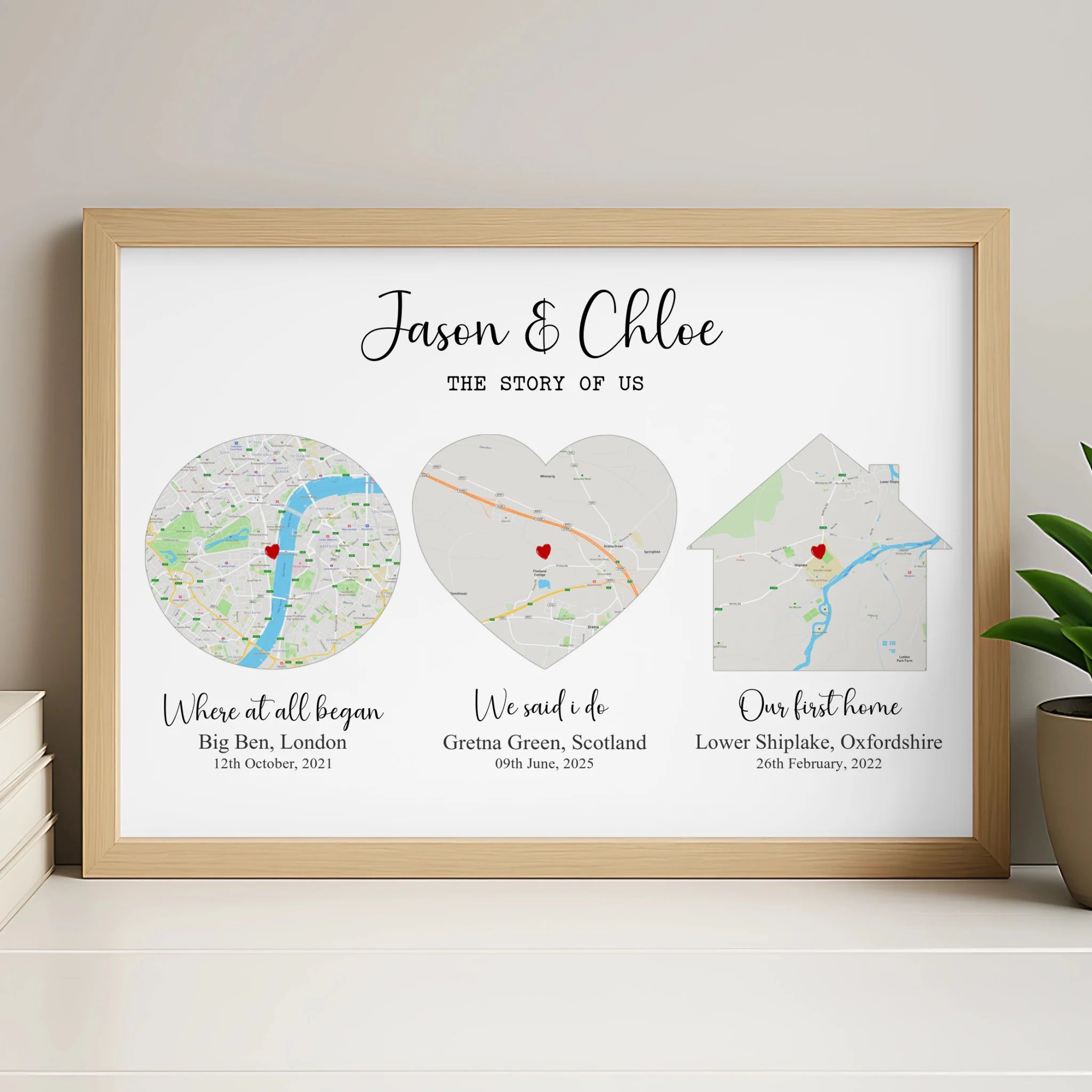 Natural wood framed Story of Us map print on a shelf beside a plant and books, three location maps in circle, heart and house