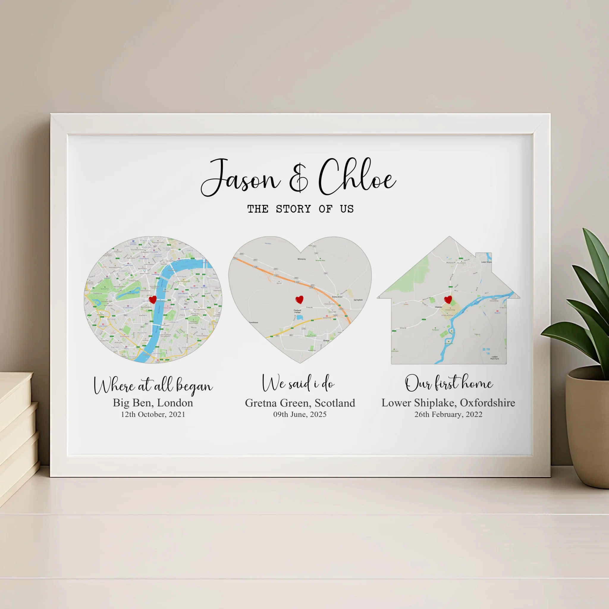 White framed Story of Us couples map print on a light shelf beside a plant, three shaped map panels with location names and d