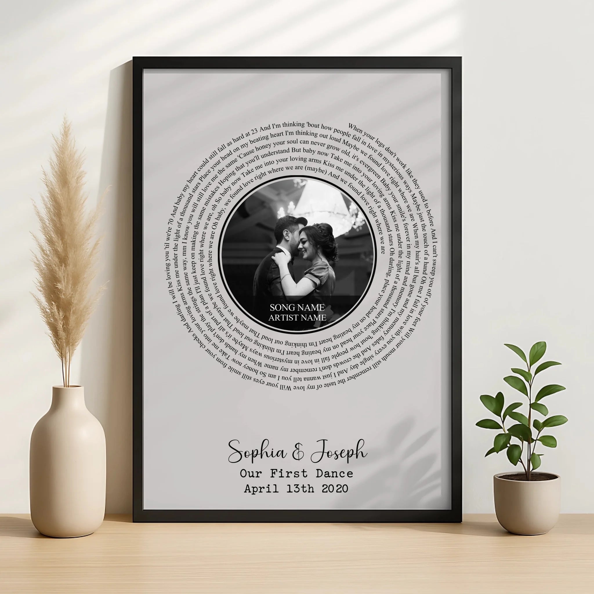Black framed spiral song lyric print on wooden surface flanked by pampas grass and a small plant, personalised for Sophia and