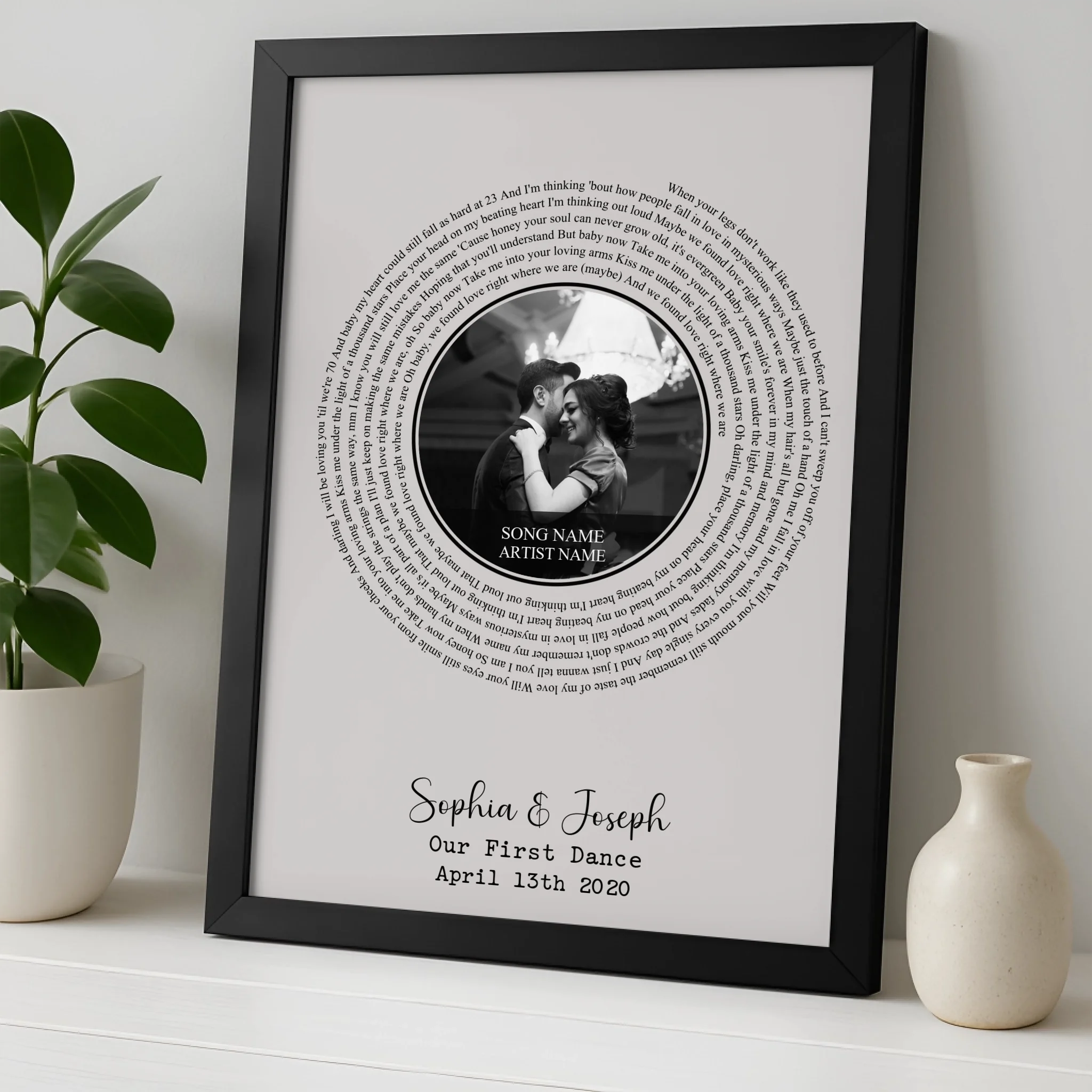 Black framed first dance song lyric print leaning on shelf, spiral lyrics around couple's black and white photo, names Sophia