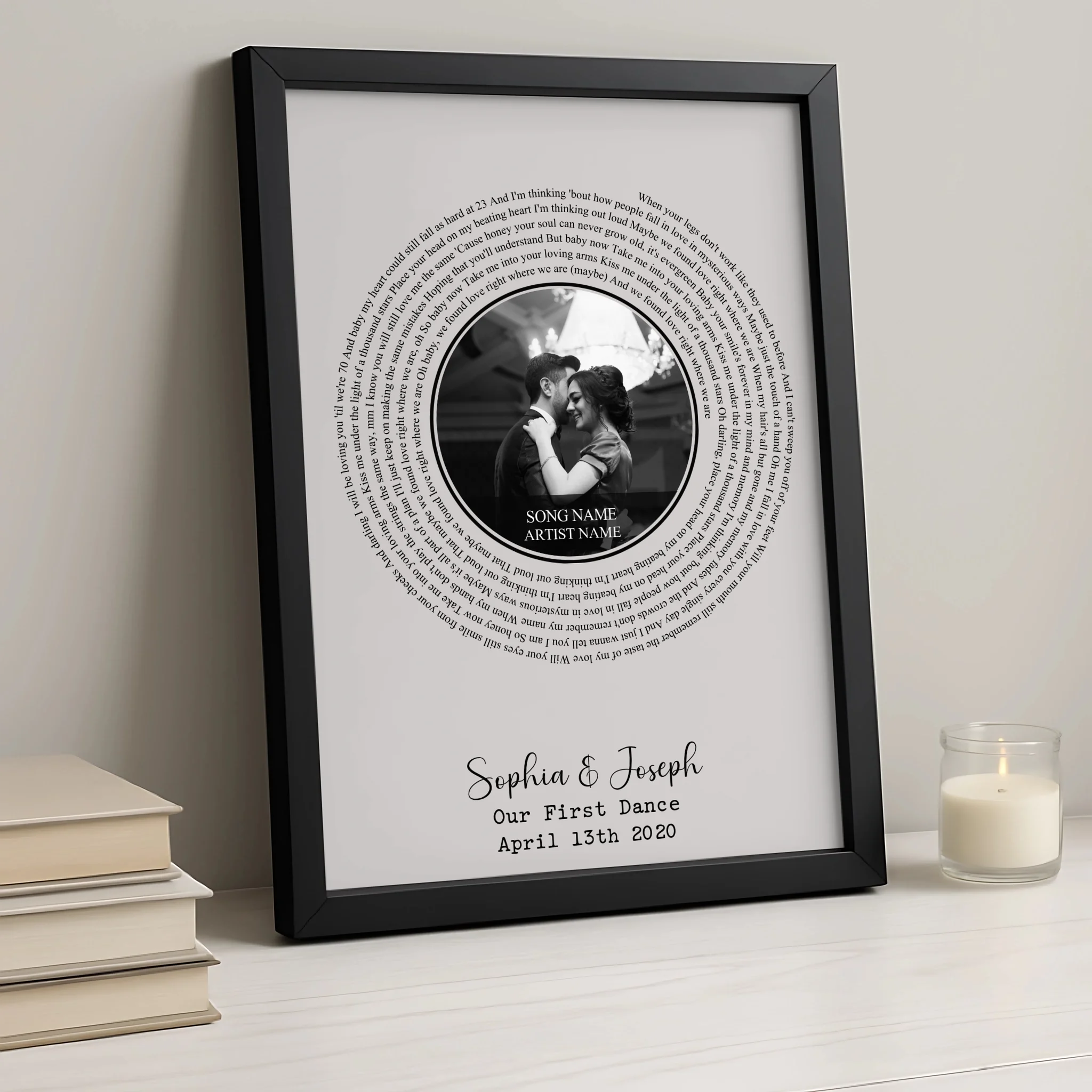 Black framed spiral song lyric print propped against stacked books beside a lit candle, personalised with Sophia and Joseph, 