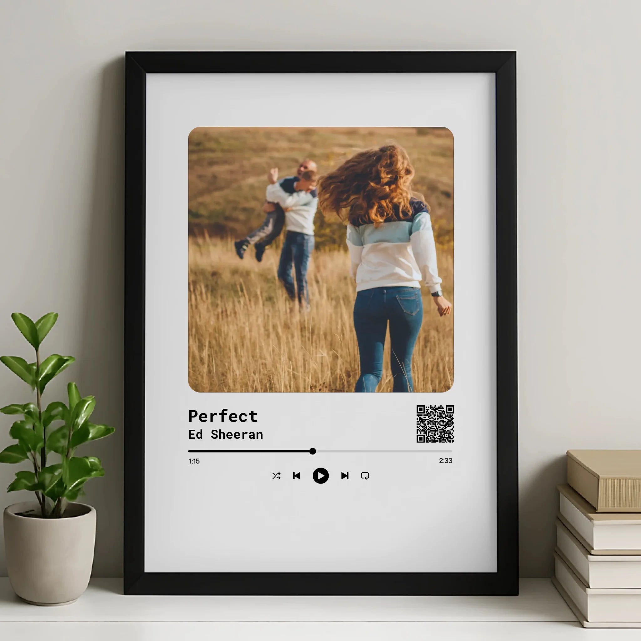Personalised song print in black frame showing couple in a field, titled Perfect by Ed Sheeran with QR code, beside a plant a