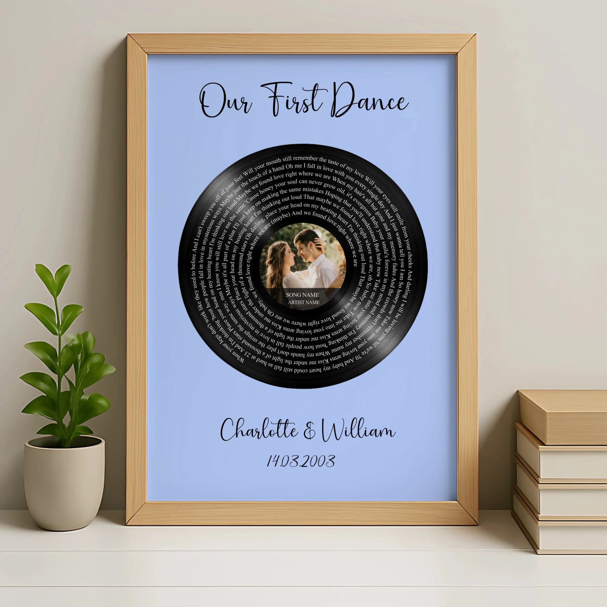 Natural wood framed personalised vinyl record lyrics print on blue, couple photo at centre, names and date below, beside plan