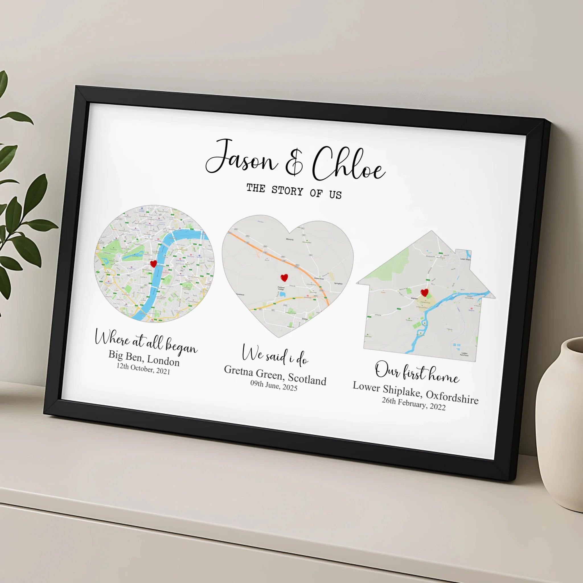 Black framed Story of Us map print leaning on a shelf beside a vase, three maps in circle, heart and house shapes with place 