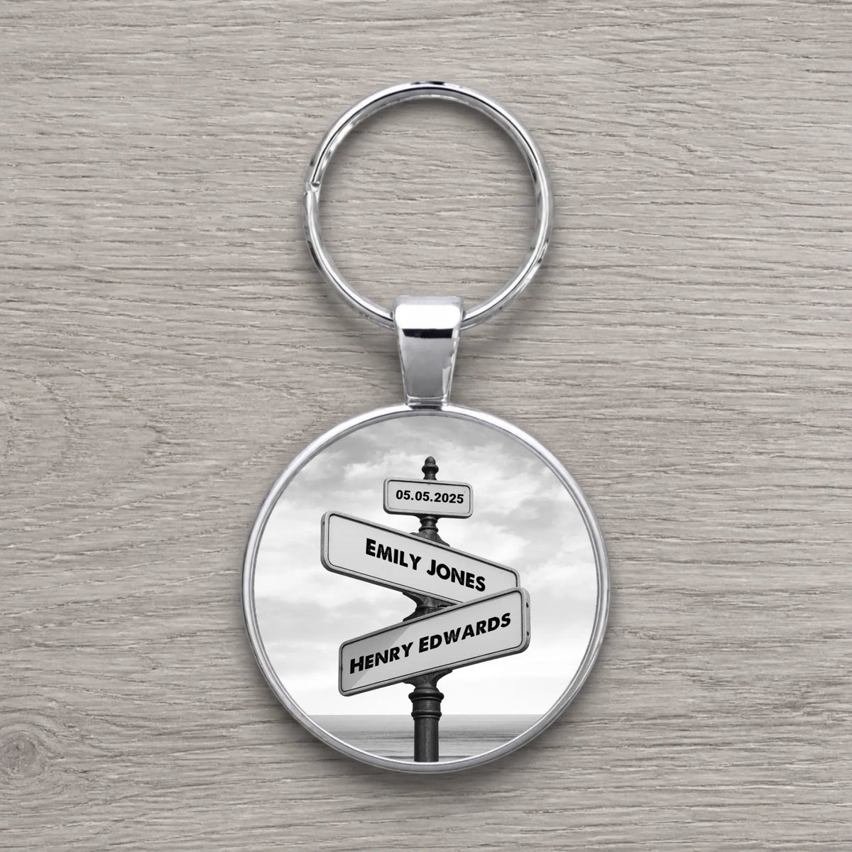Round silver keyring featuring a black and white vintage crossroads street sign personalised with Emily Jones, Henry Edwards 